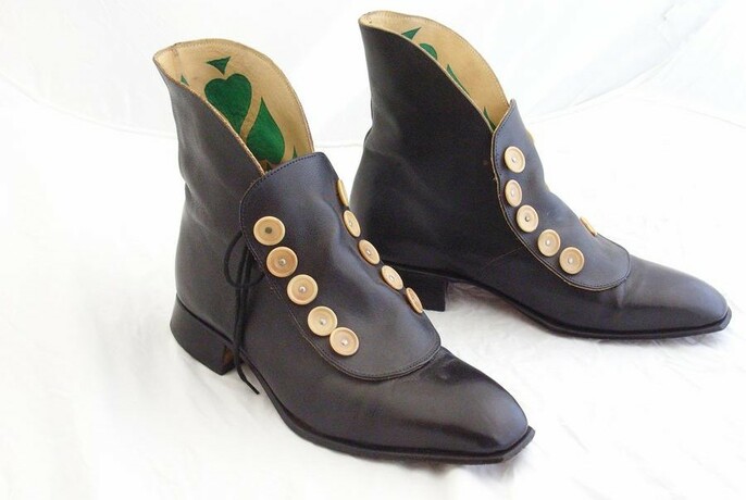 Pair of black leather handmade boots with many gold buttons on them.