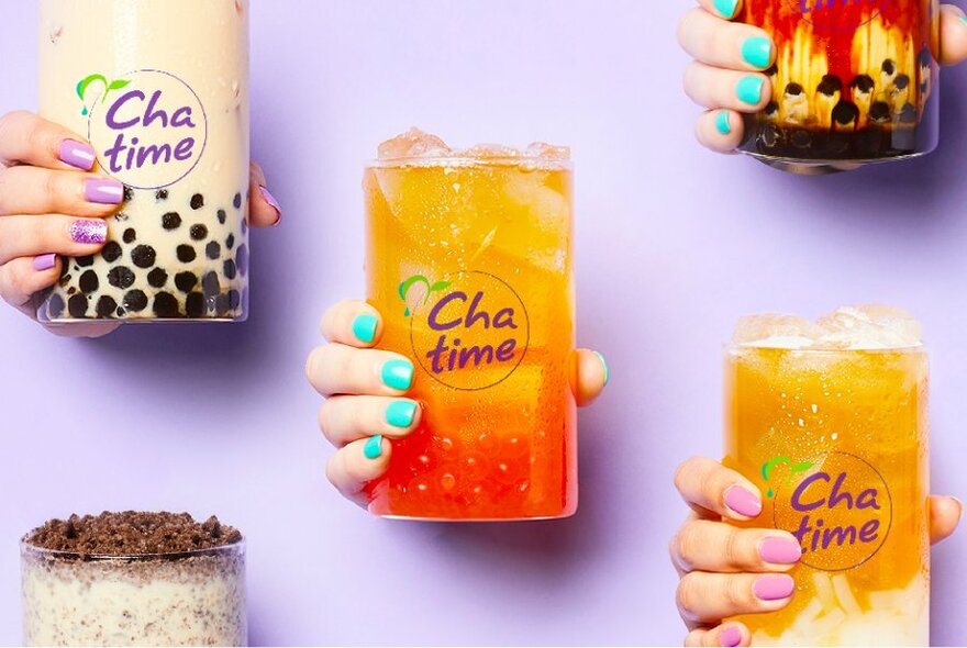 Hands holding different kinds and colours of bubble tea, the glasses printed with the words 'Cha time' on the outside.