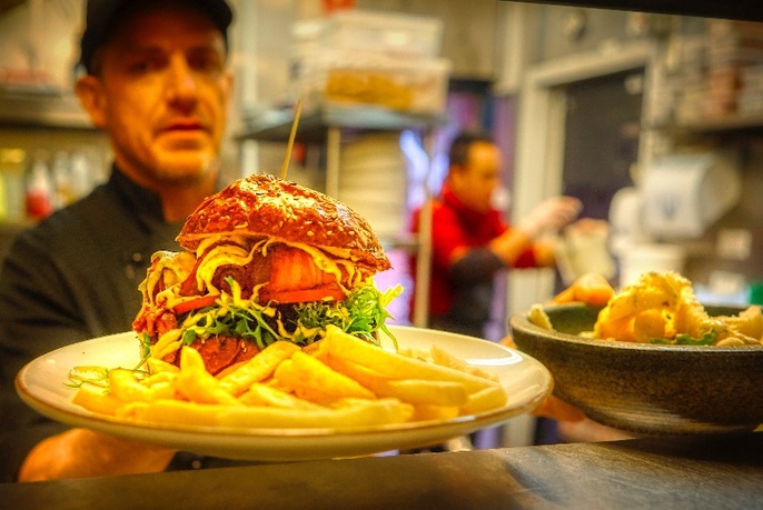 Chef holding up a plate with a burger and chips.