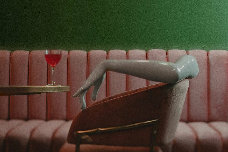 A red cocktail next to a quirky chair with a decorative arm draped across the back. 