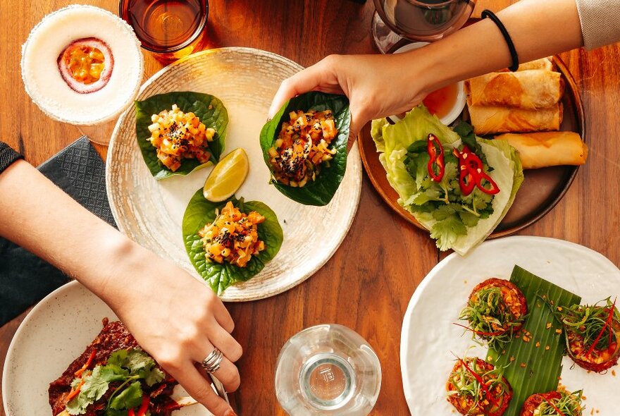 People reaching for Asian share dishes and cocktails in a restaurant.