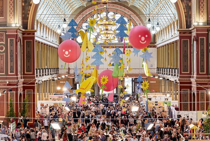 Birds-eye view of the interior of Royal Exhibition Buildings filled with crowds of people browsing stalls, with colourful Christmas decorations suspended from the ceiling.