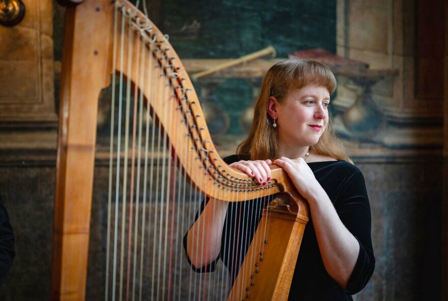 Harpist Hannah Lane seated with her hands on her instrument, wearing black and looking to the side.