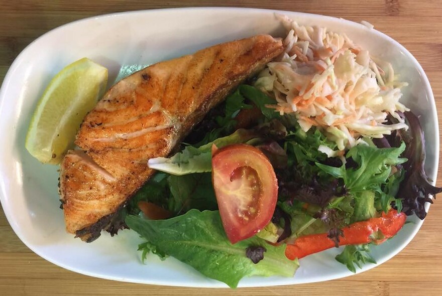 A plate of grilled fish with green salad and coleslaw.