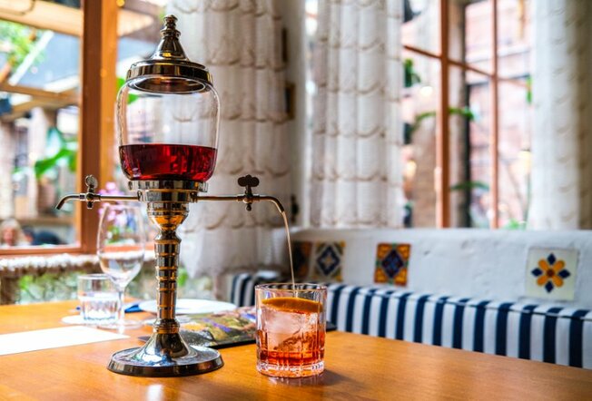 A drink is poured from a negroni fountain in a sunny restaurant. 