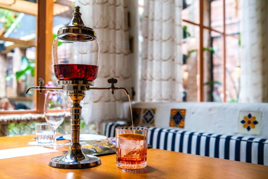 A drink is poured from a negroni fountain in a sunny restaurant. 