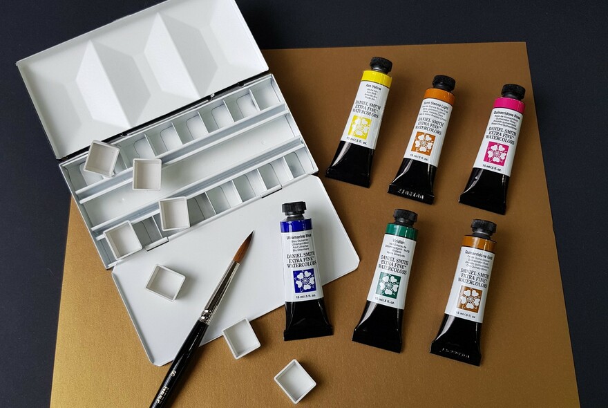 Six tubes of watercolour paints, an artist paintbrush and a watercolour mixing tray.