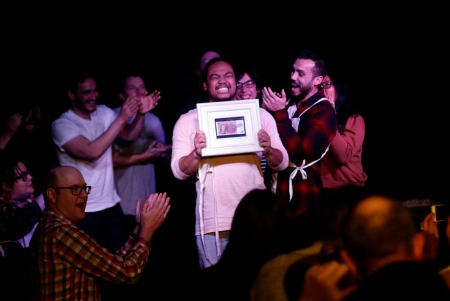 Group of people on a stage applauding a person holding a framed picture.