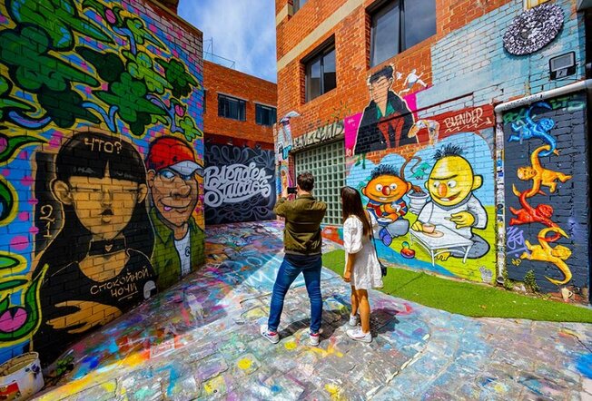 A couple in a laneway with colourful street art murals. 