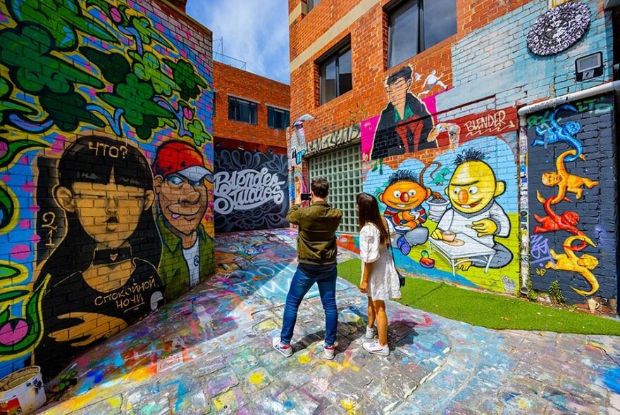 A couple in a laneway with colourful street art murals. 
