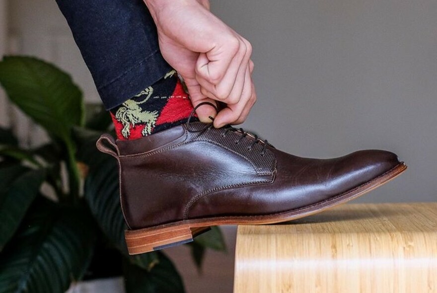 Detail of men's brown shoe being tied, with red Argyle socks.
