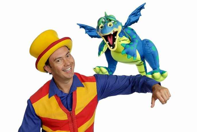 Magician Tim Credible wearing a red and yellow striped vest and hat, with Douzie the Dragon puppet on his arm.