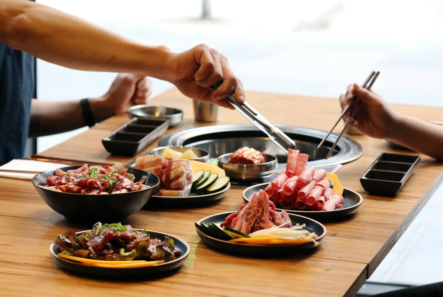 Person selecting a piece of raw meat to grill at the table in a Korean barbeque.