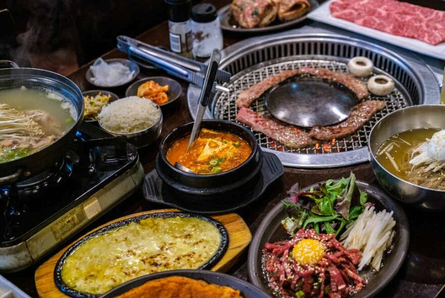 Various Korean meat and vegetable dishes next to a hot grill