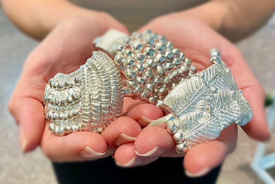 Three large, stunning pieces of silver jewellery being held in the palm of a woman's hand.