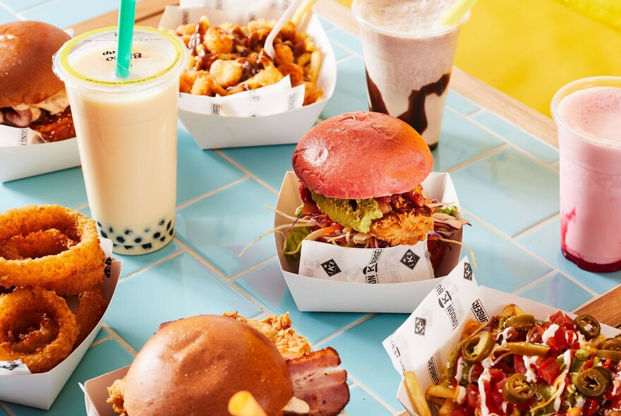 Blue-tiled table topped with burgers in boxes, onion rings and milkshakes.