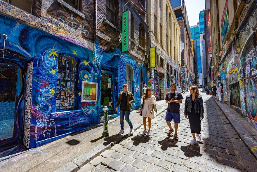 A group of people walking down a street art covered laneway. 