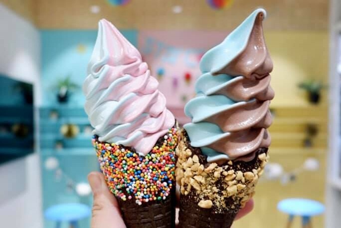 Two swirls of soft-serve ice cream in cones dipped in chocolate, sprinkles and nuts.