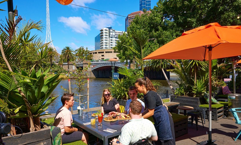 A group of friends dining at a table beside the yarra river.