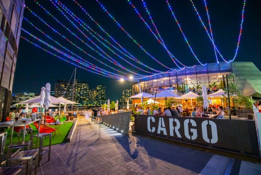 Night shot of outdoor dining with white umbrellas under blue fairy lights.