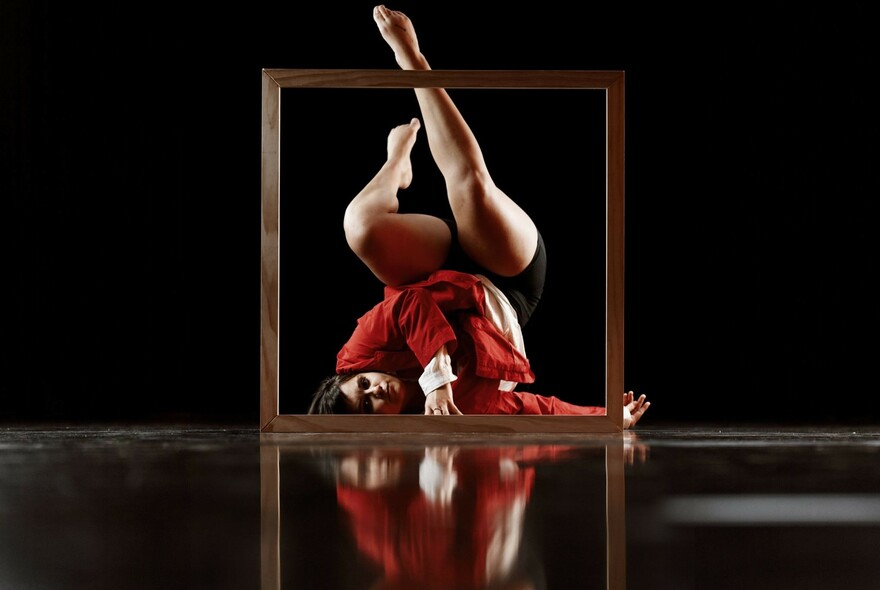 Dancer wearing red lying on her back on the floor with legs stretched upwards.