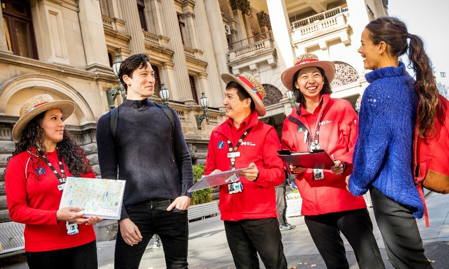 City of Melbourne volunteers in red jackets laughing with two visitors outside Melbourne Town Hall.