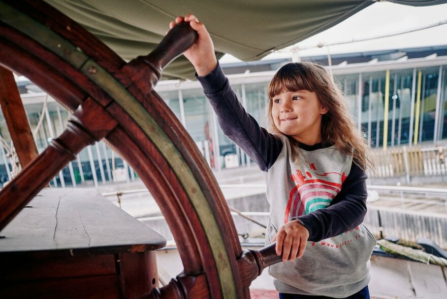 A young girl holds an old ship steering wheel.