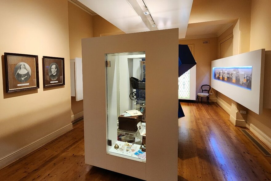 Display of photographs on the walls and objects in a glass display cabinet in a room at the Mary MacKillop Heritage Centre.