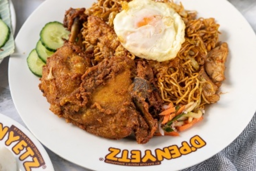 Fried chicken, an egg and crispy noodles served on a plate with the words D'Penyetz written in yellow on the plate's white rim.