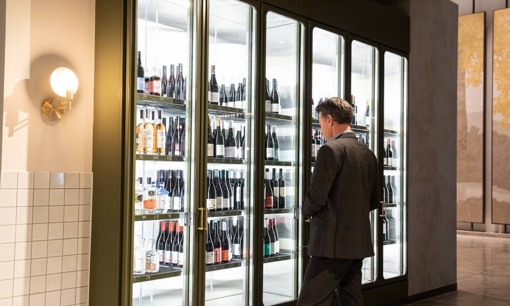Man browsing wine bottles in a fridge at a bottle shop. 