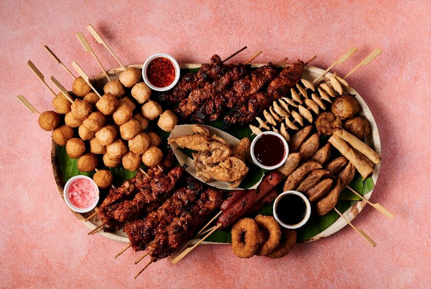 A platter of meat and vegetable on skewers, with dipping suace.