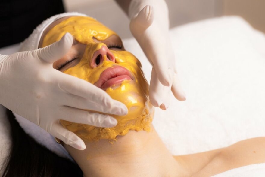 A customer receiving a yellow facial mask treatment.