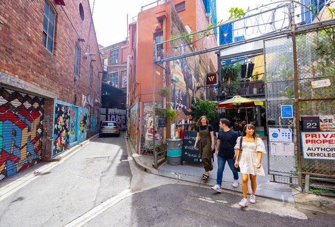Three people exiting an outdoor laneway bar. 