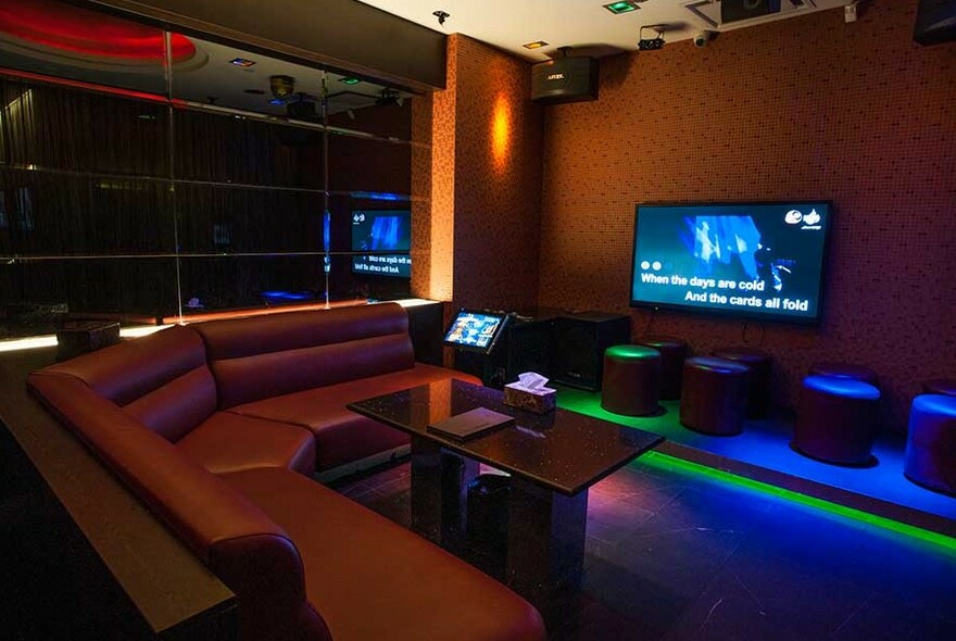 Karaoke room with large TV screen and long couch.