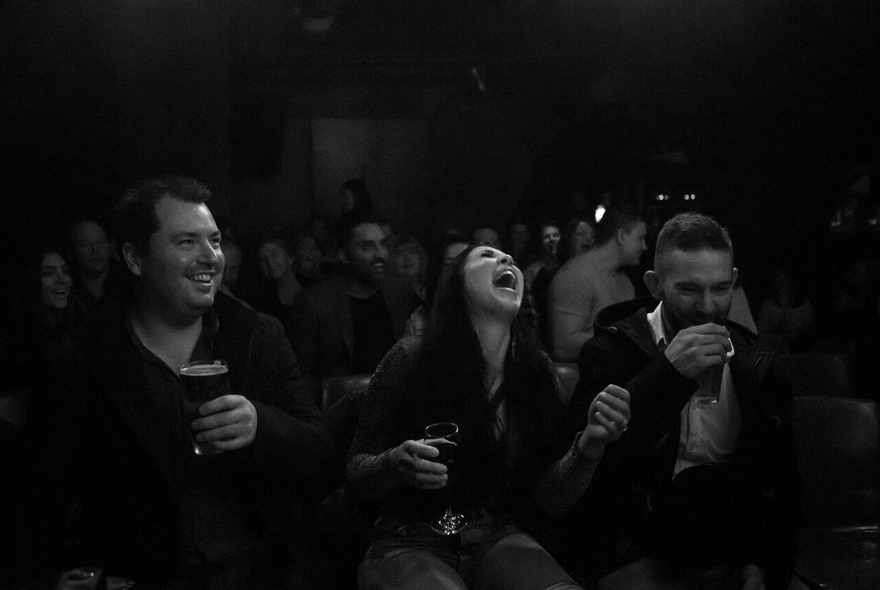 Three people holding drinks, laughing and sipping.