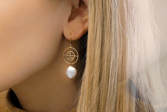 Model wearing a Francesca logo gold and pearl drop earring.
