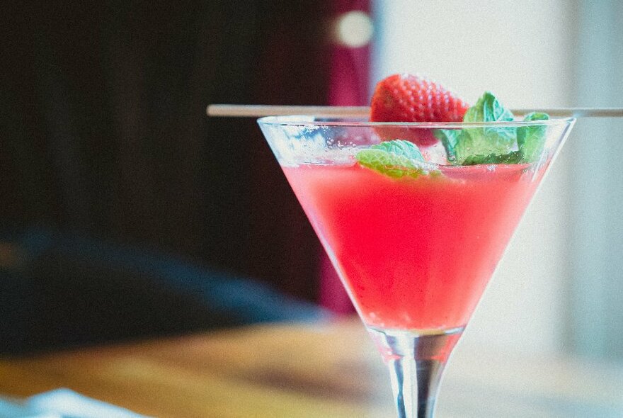 Red-coloured cocktail with a garnish of strawberry and mint.