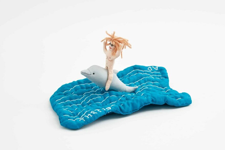 A small sculpture of a wild-haired woman riding a dolphin in waves. 