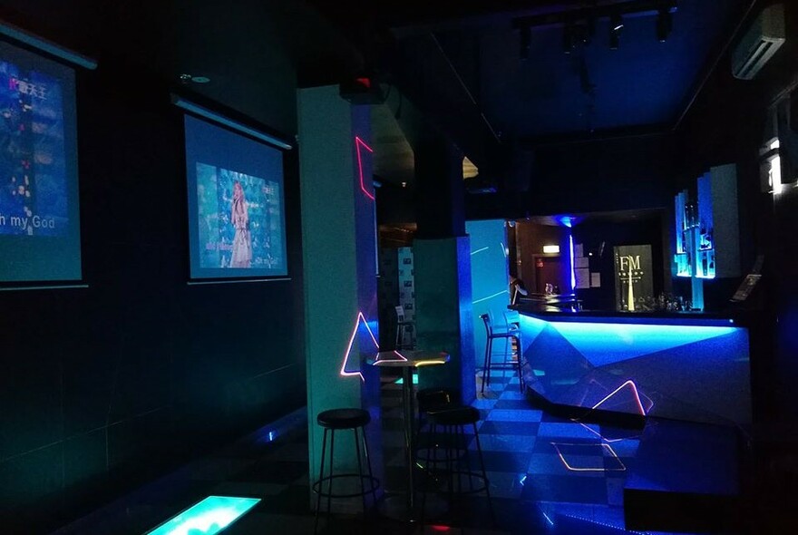 Karaoke bar with screens and blue lighting.