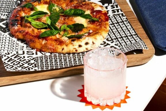 Pizza on a tray with a cocktail in the foreground.