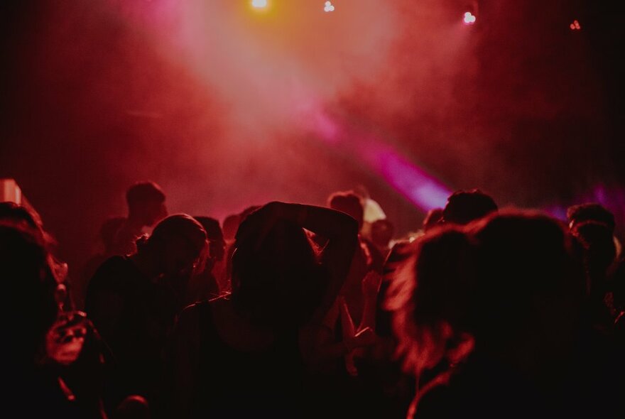 People dancing in a dark nightclub with red lights.