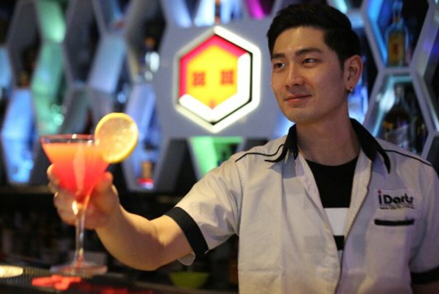A bartender raises a red cocktail glass.