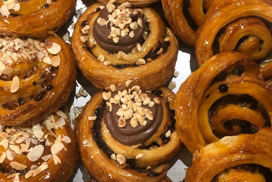 Rows of scrolls topped with flaked almonds and chocolate with nuts.