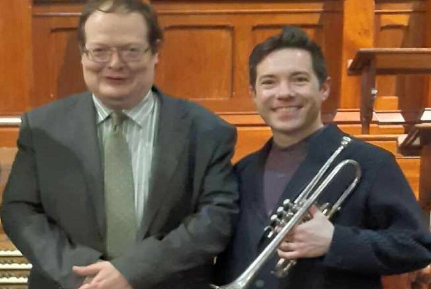 Two musicians, one holding a trumpet, smiling in a church setting.