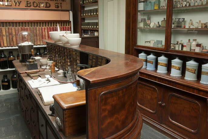 Old-fashioned wooden chemist's counter with cabinets containing jars behind.