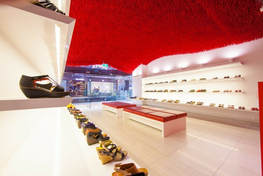 Camper shop interior with rows of shoes, central benches and red ceiling.