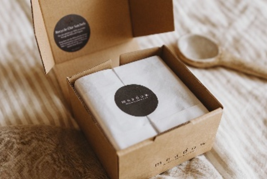 An opened box showing white tissue paper inside with a black circular sticker with a wooden spoon in the background. 