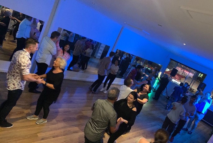 An angled image of people dancing in pairs in a blue-lit room.