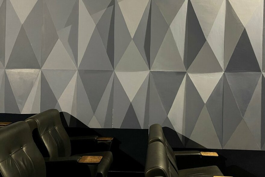 Three dimensional and textured wall surface of one of the cinemas at Cinema Nova, with large black seats in foreground. 