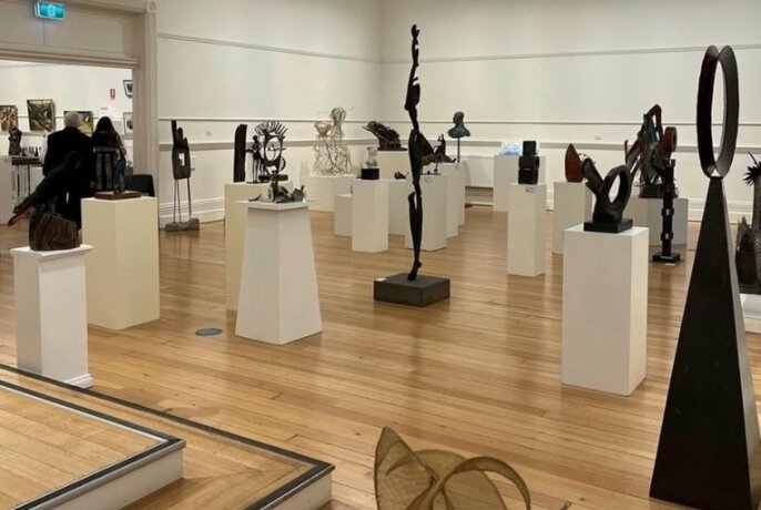 A gallery space with timber floors, white walls and many metal sculptures on white plinths.